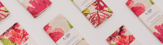 A photograph, taken from above, of seaweed printed tea towels folded in their paper packaging