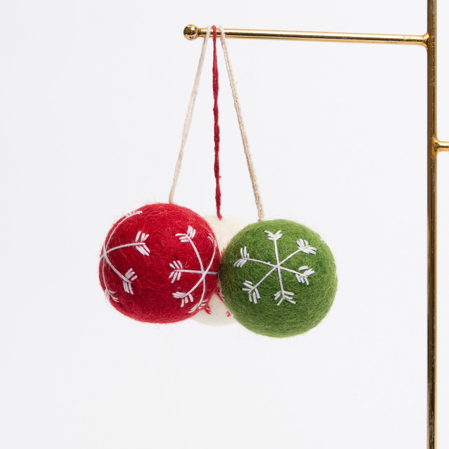 Three felt Christmas bauble decorations hanging on a metal rod. They are white, red, and green, with snowflake stitching on the face of each.