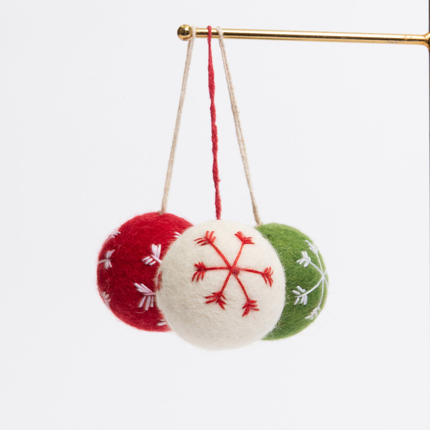 Three felt Christmas bauble decorations hanging on a metal rod. They are white, red, and green, with snowflake stitching on the face of each.