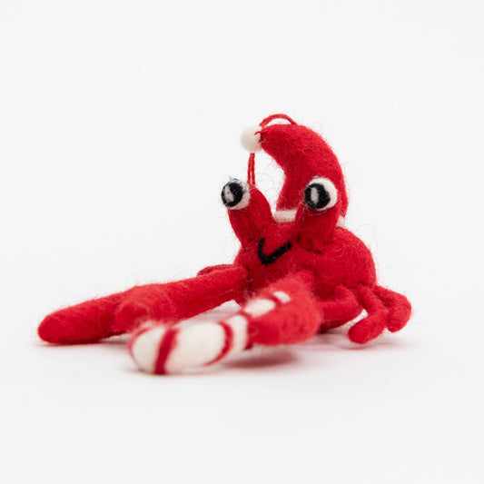 A Christmas crab decoration pictured on a white background. The felt crab is red and is wearing a Christmas hat.