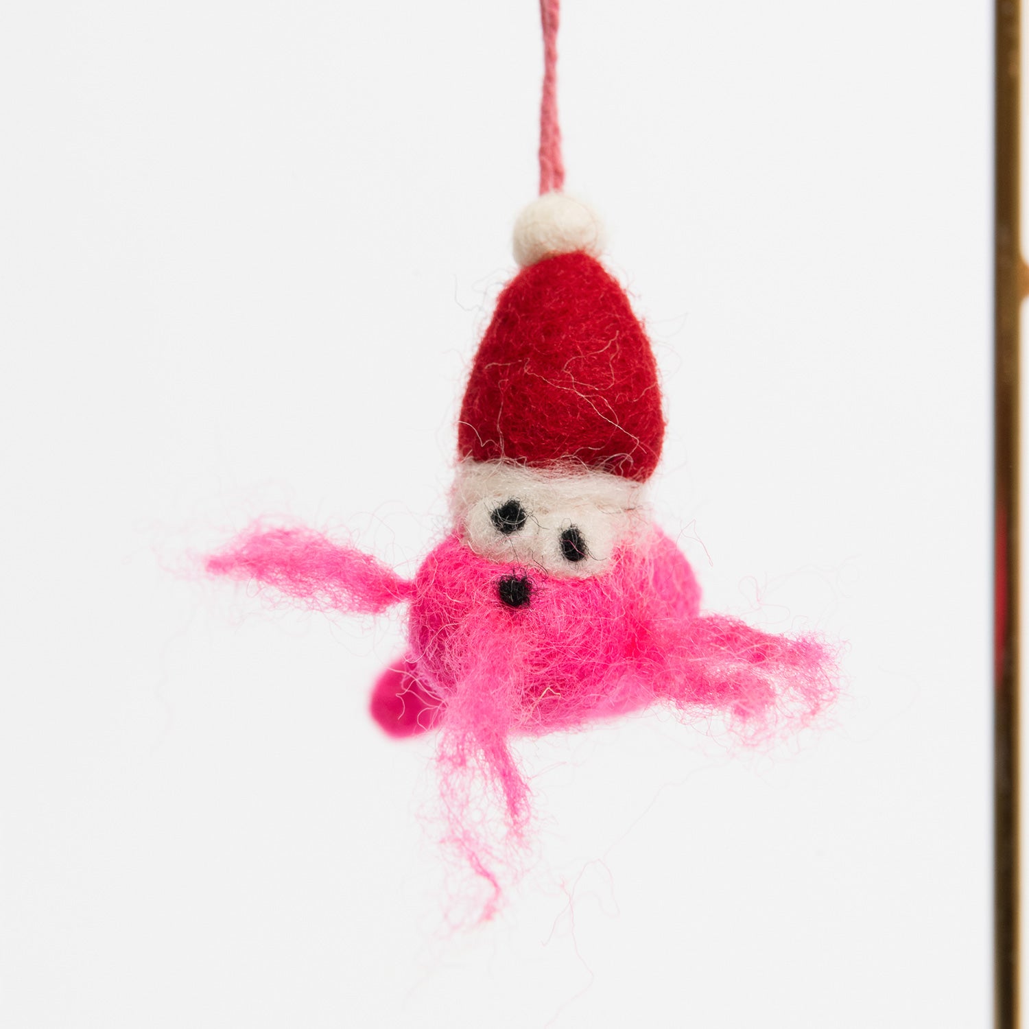 A Christmas decoration hanging on a metal rod on a white background. The decoration is a festive pink prawn wearing a Christmas hat.