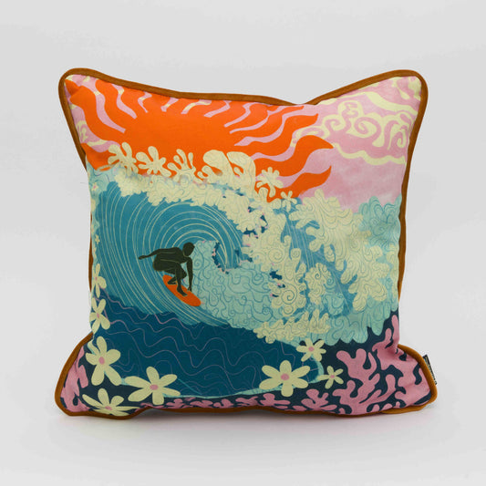 Square cushion showing a surfer riding a big turquoise wave with flowers as foam and coral under the sea. a pink sky with a big red sun in the background.