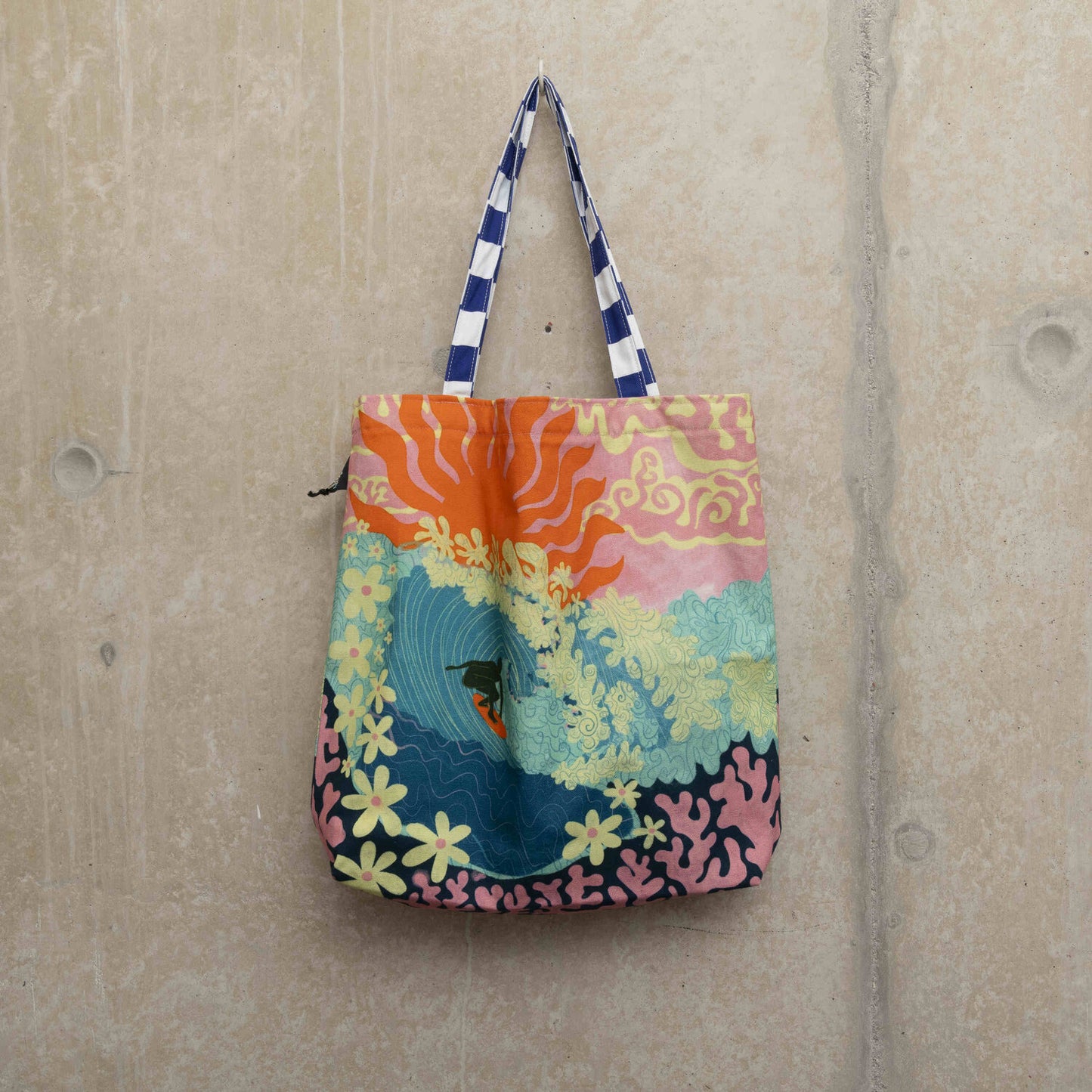 Large tote bag showing a surfer riding a big turquoise wave with flowers as foam and coral under the sea. a pink sky with a big red sun in the background