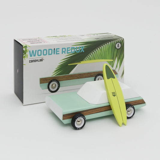 Shot of mint green and white wooden car with wooden surfboard leaning against the car. Shot in front of its box