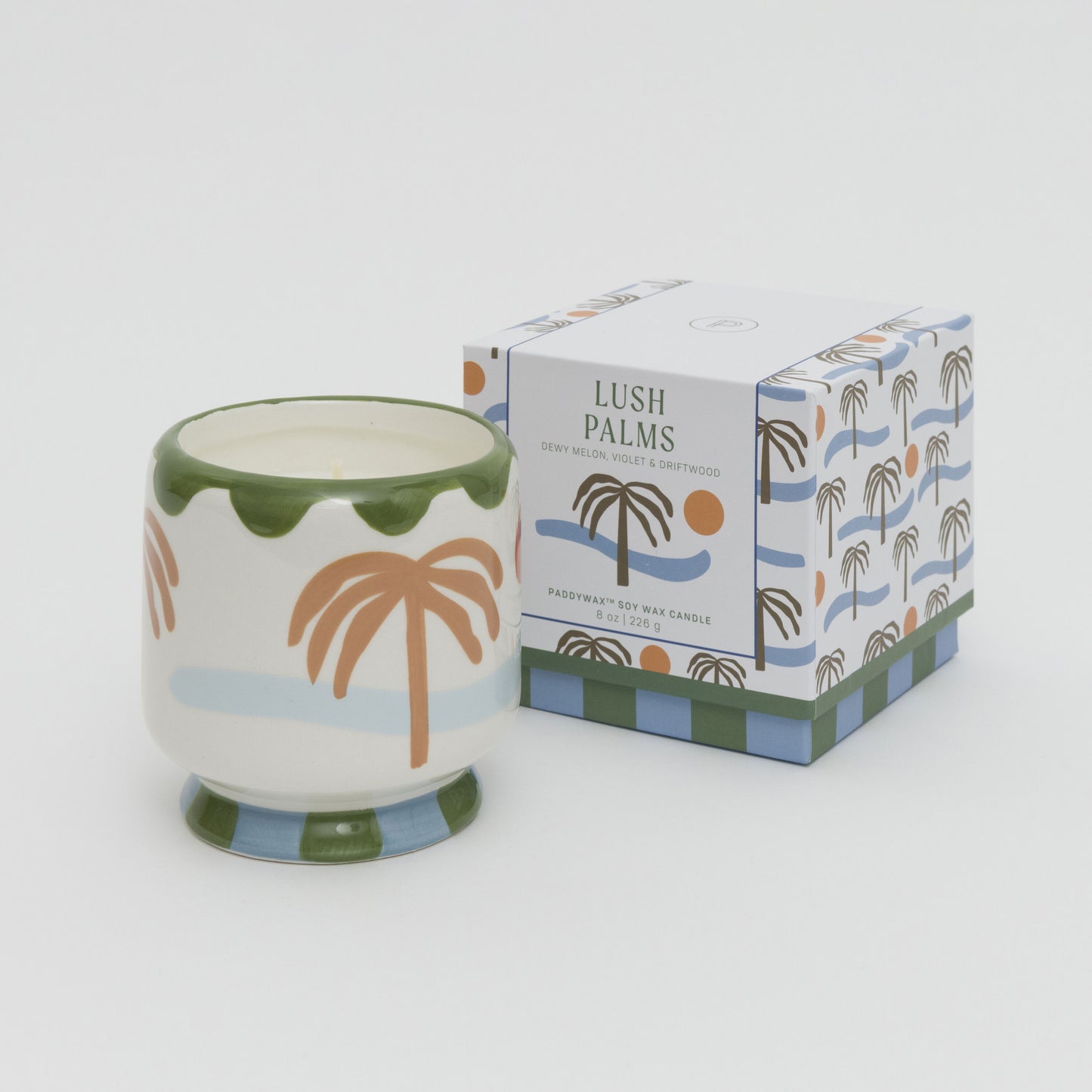 Image of soy candle in a ceramic candle holder painted with palm tree, sea and sun. Candle is placed next to the square box with matching artwork.