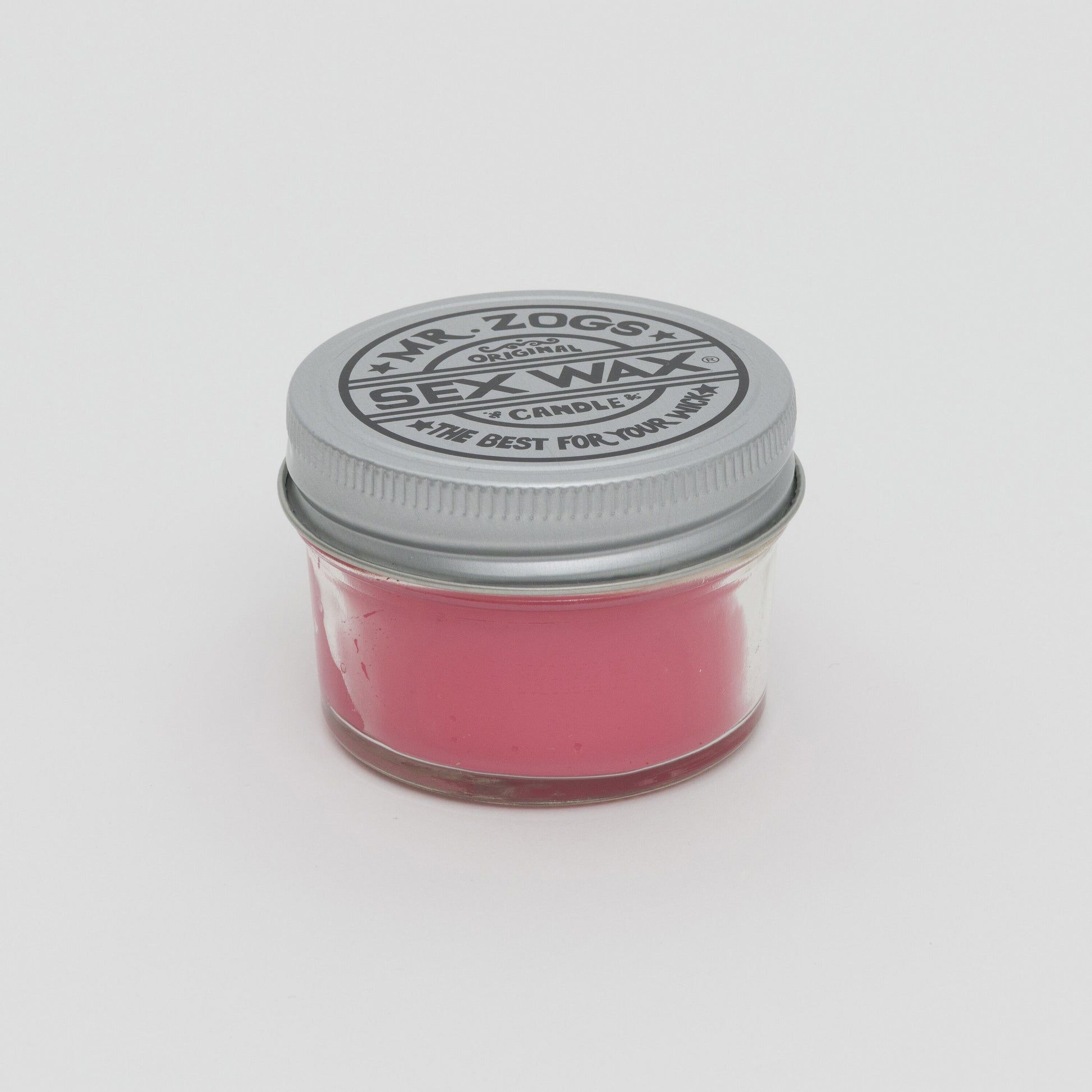 Side shot of pink candle in a glass jar with screw top lid.