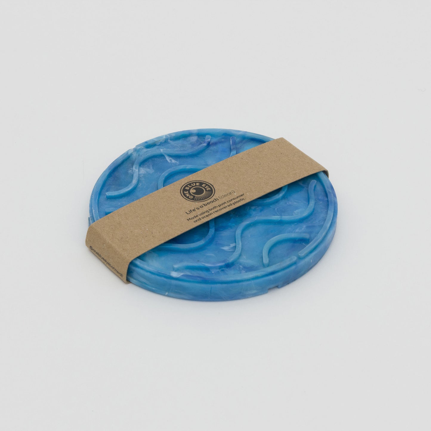 Shot of blue circular soap dish with wave shaped ridges to grip the soap. With cardboard belly band packaging.