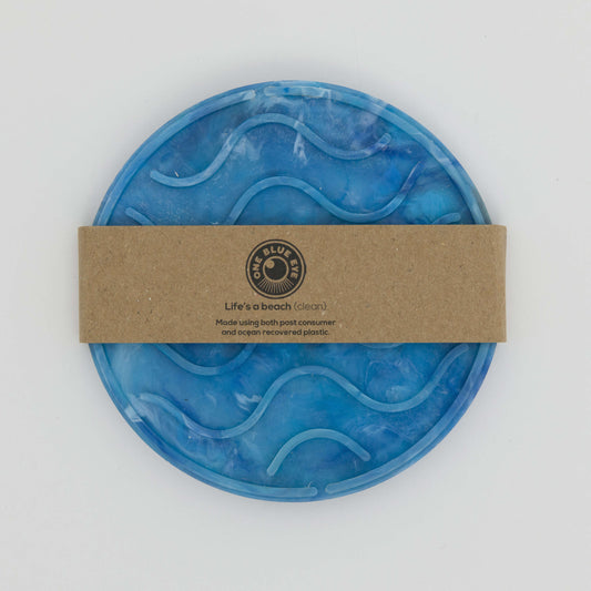 Top shot of blue circular soap dish with wave shaped ridges to grip the soap. With cardboard belly band packaging.