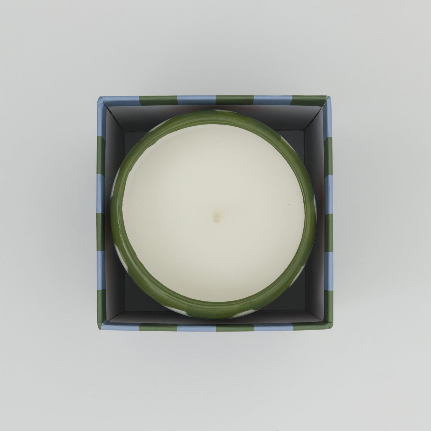 Shot from above showing white candle in its ceramic pot in its square box.