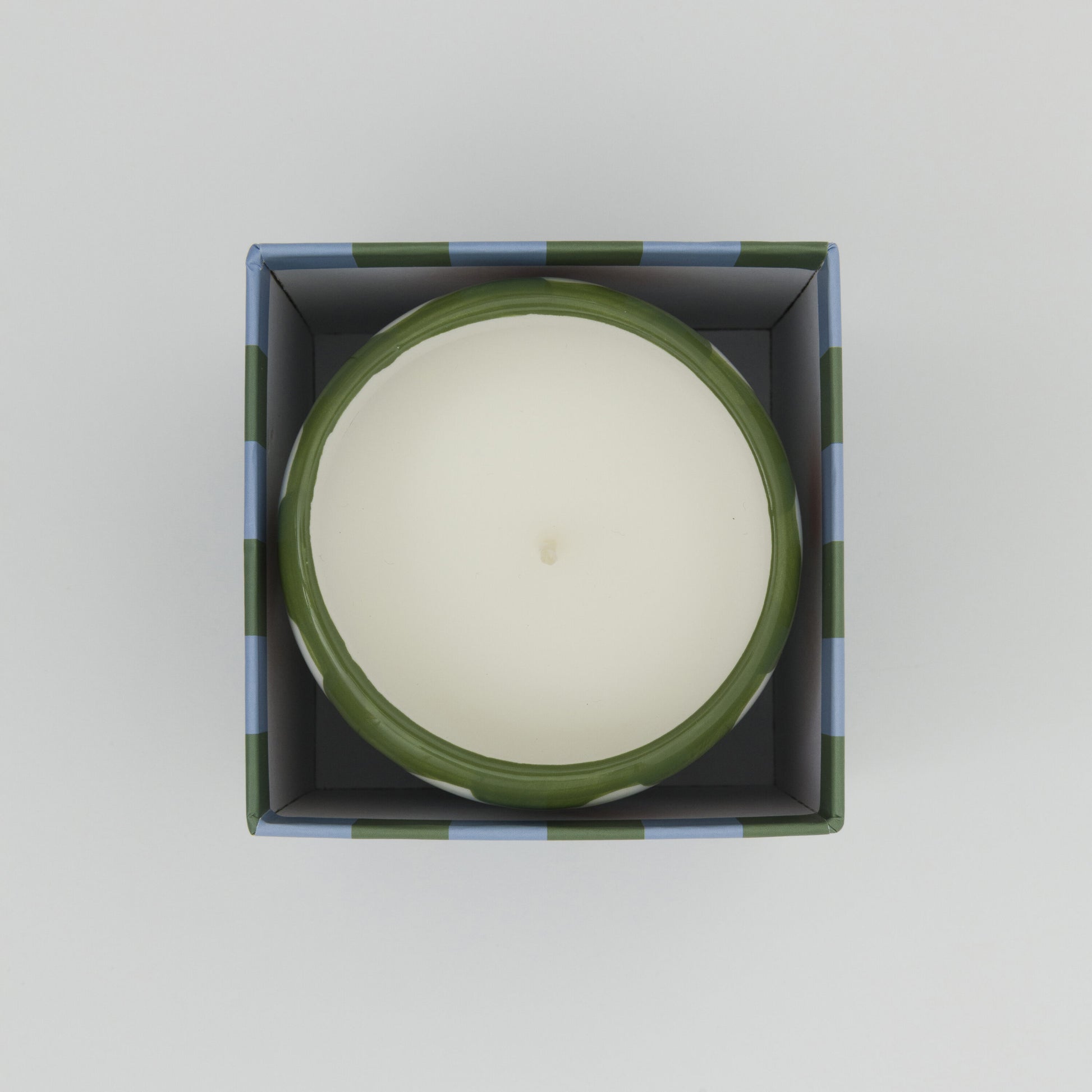 Shot from above showing white candle in its ceramic pot in its square box.