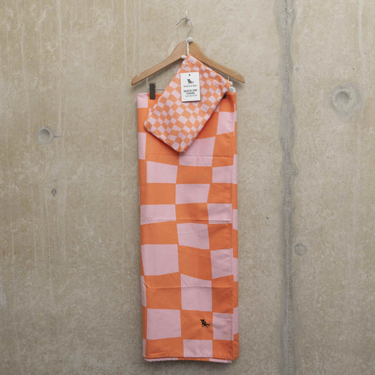 Pink and orange checkerboard beach towel on a hanger with carry pouch hooked onto the hanger.