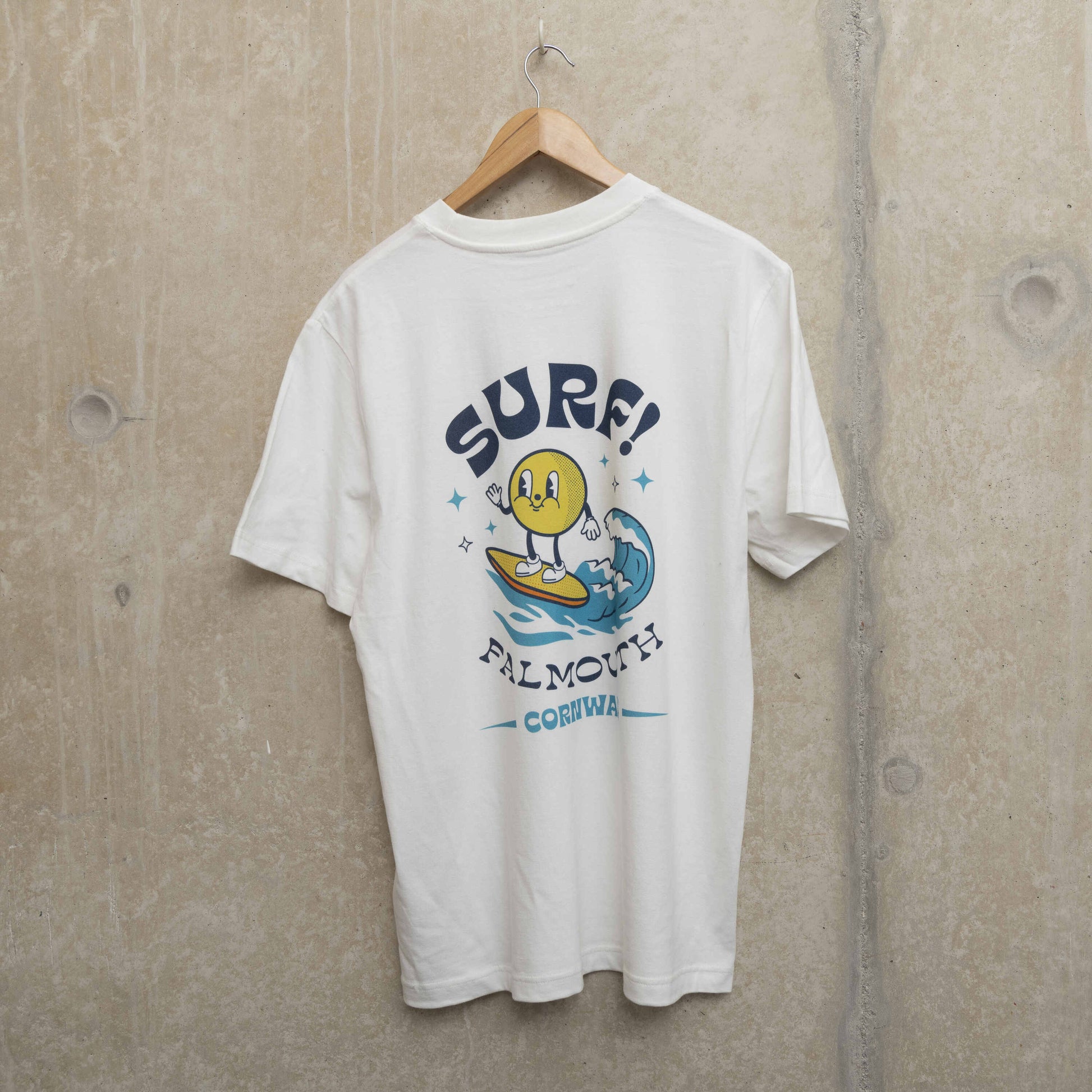 Back shot of white t-shirt with large surf motif across the back. Motif shows round character surfing a wave with the wording SURF! Falmouth, Cornwall.