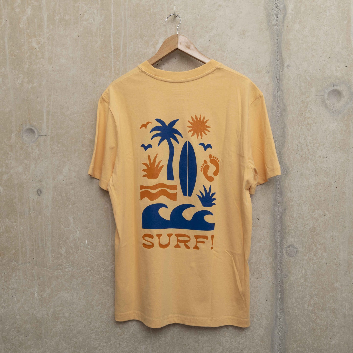 Back shot of large motif on the back of the light yellow t-shirt. Motif shows waves, foot prints, surfboard, sun and palm tree in navy and orange.