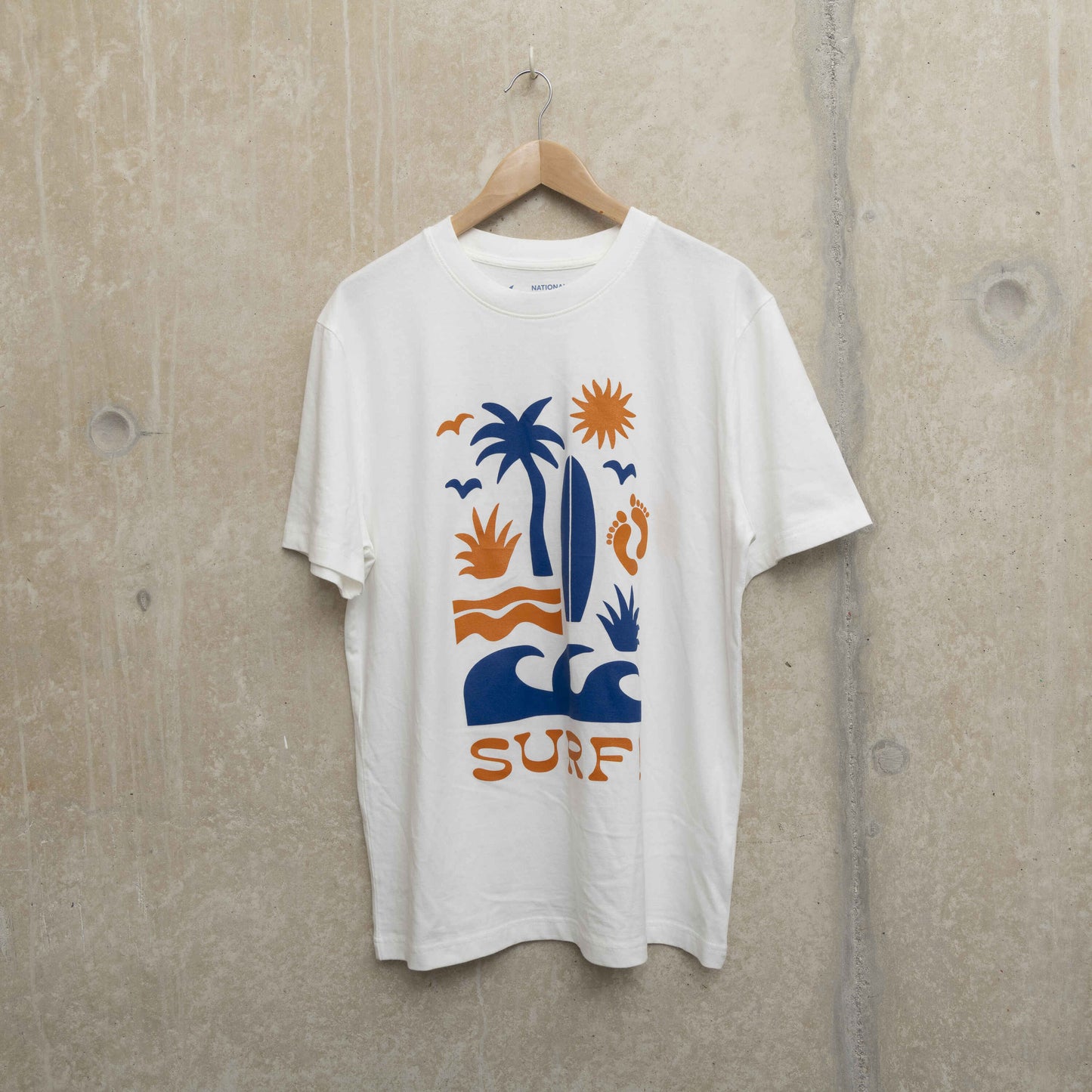 Front shot of white t-shirt with Surf motif. Motif shows waves, foot prints, surfboard, sun and palm tree.