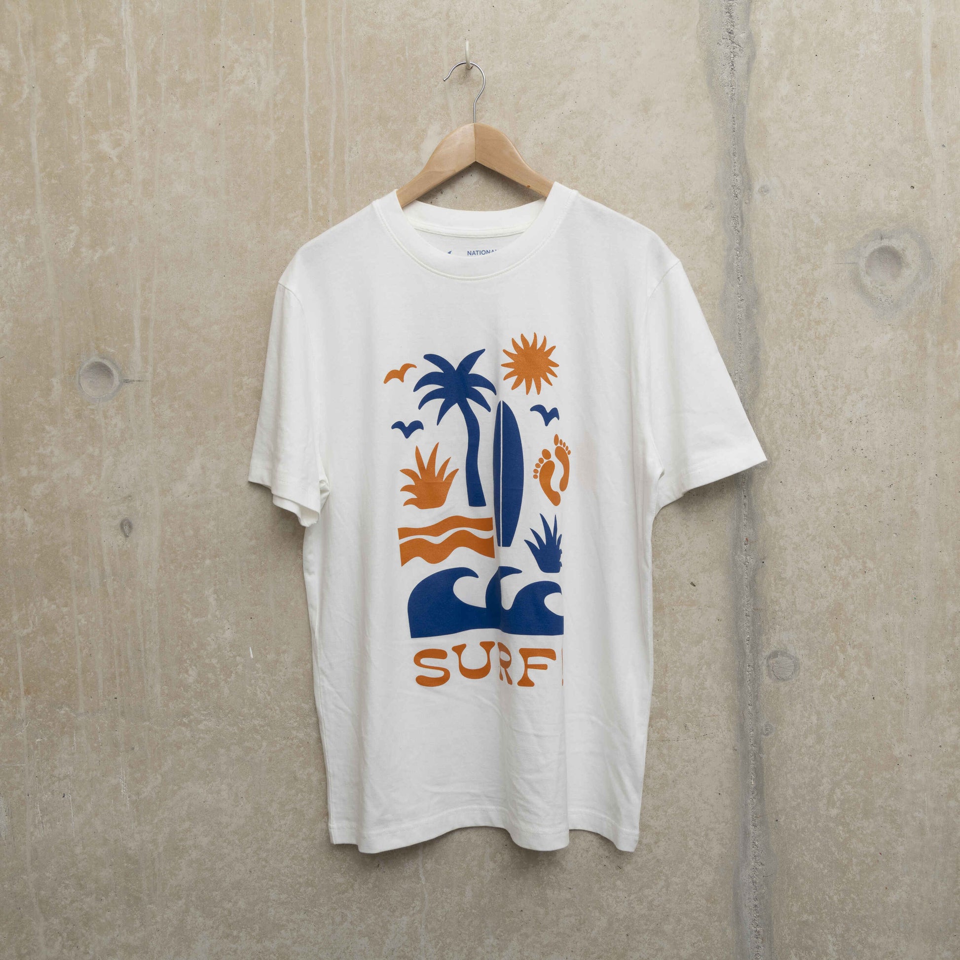 Front shot of white t-shirt with Surf motif. Motif shows waves, foot prints, surfboard, sun and palm tree.