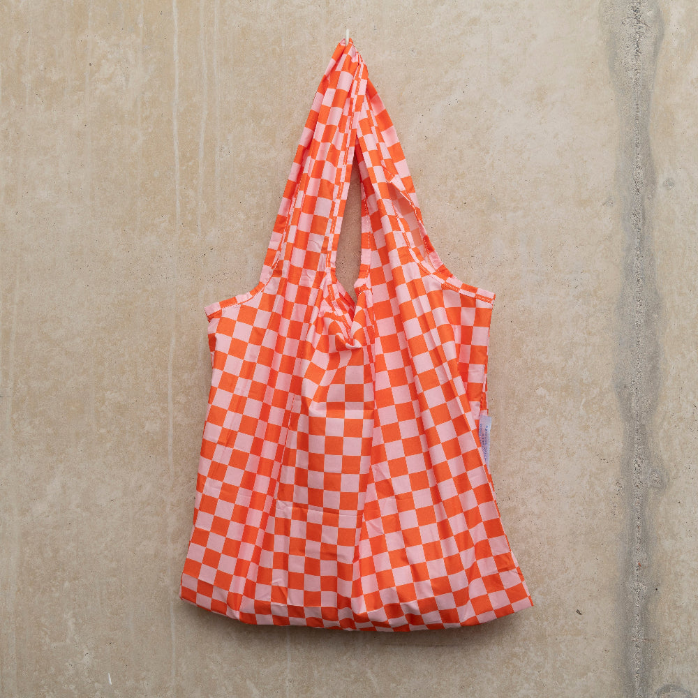 Image of checkerboard design bag in pink and orange, hanging on a hook against a concrete wall.