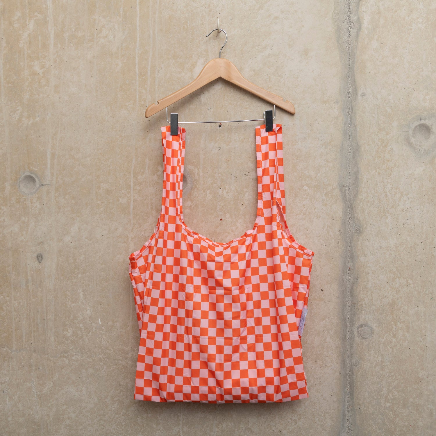Image of checkerboard design bag in pink and orange, hanging on a wooden hanger against a concrete wall.