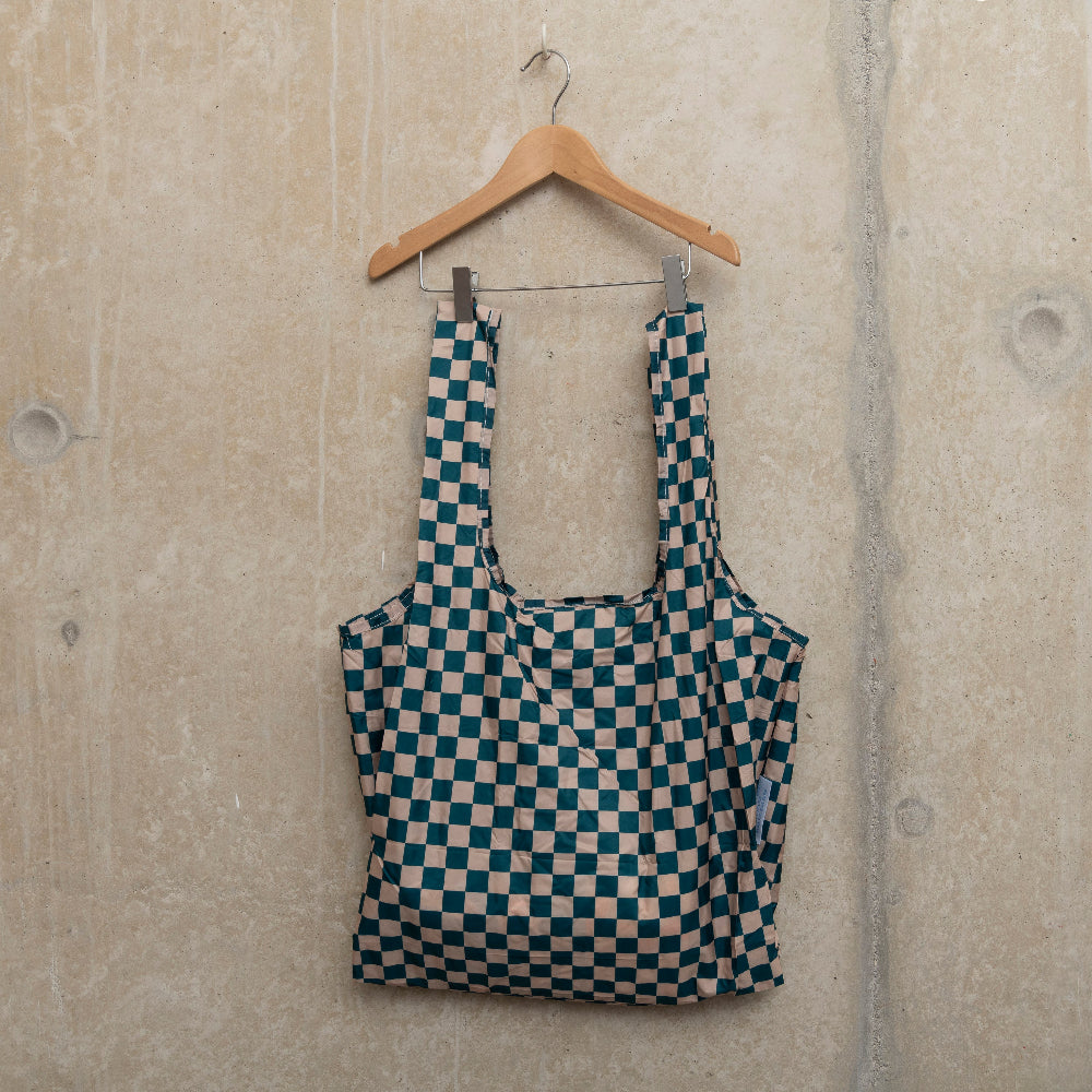 Image of checkerboard design bag in teal and beige, hanging on a hanger against a concrete wall