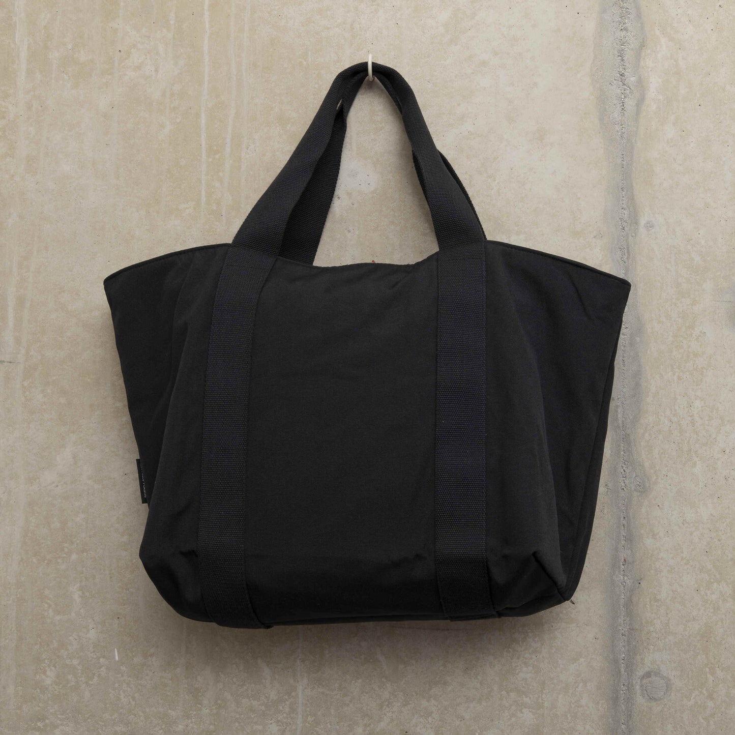 Showing the back of a black tote bag with sturdy handles