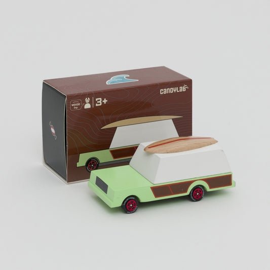 Shot of mint green and white car with wooden surfboard on the roof. Shot in front of its box