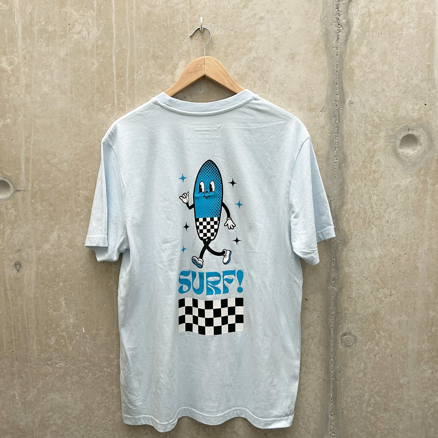 A pale blue t-shirt with a smiling surfboard cartoon icon hangs on a wooden clothes hanger