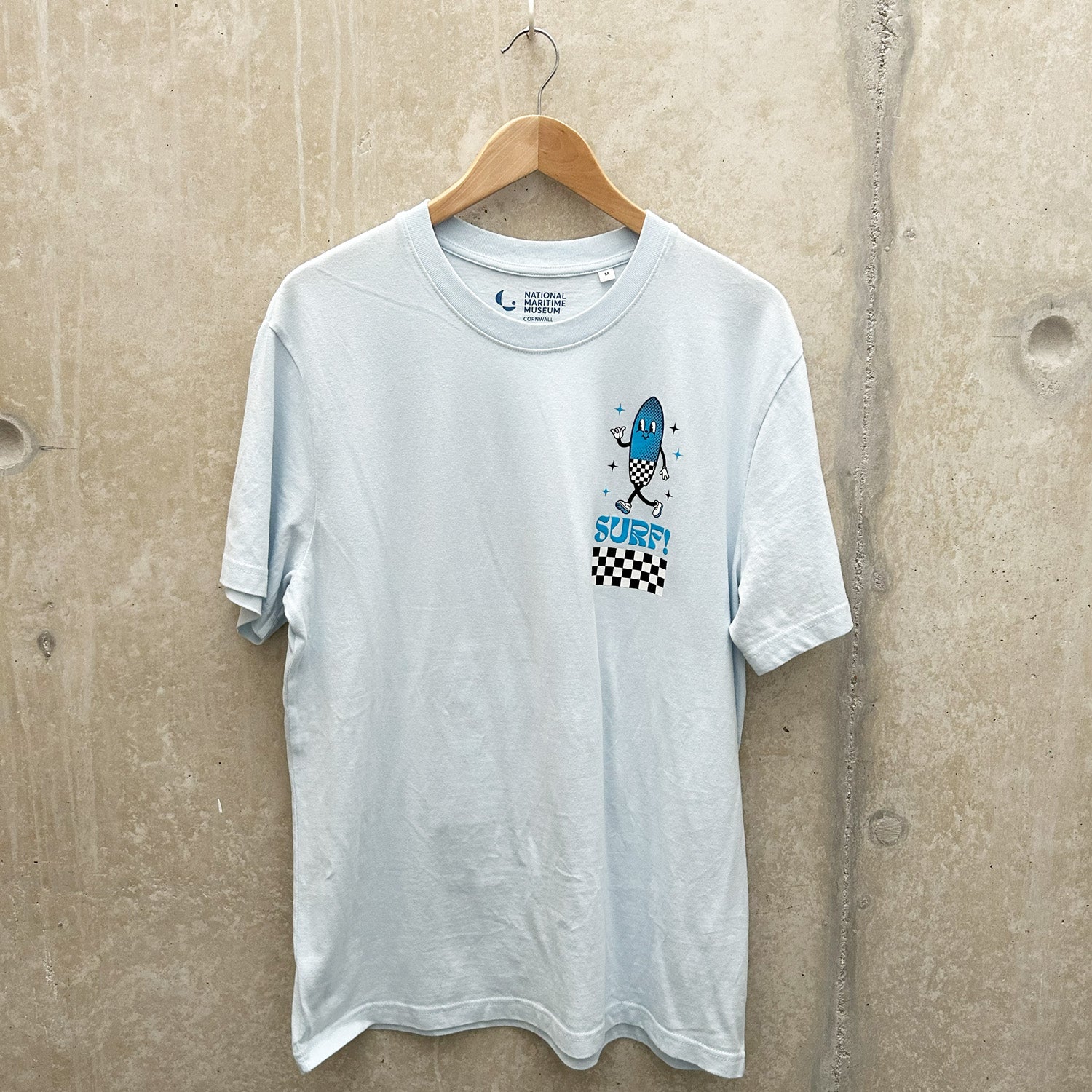 A pale blue t-shirt with a smiling surfboard cartoon icon hangs on a wooden clothes hanger