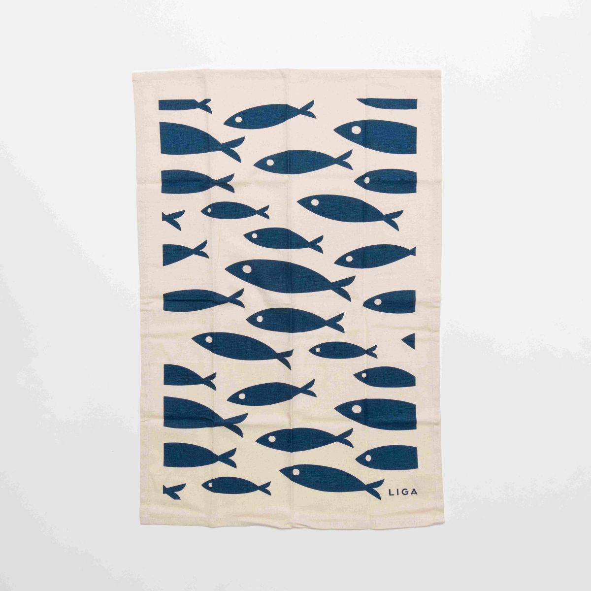 Beige towel with blue fish pattern and 'LIGA' branding on a creamy white background.