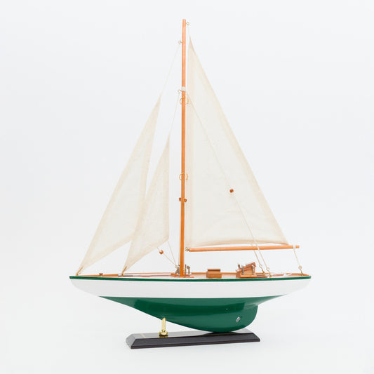Model sailboat with green hull and white sails on a white background