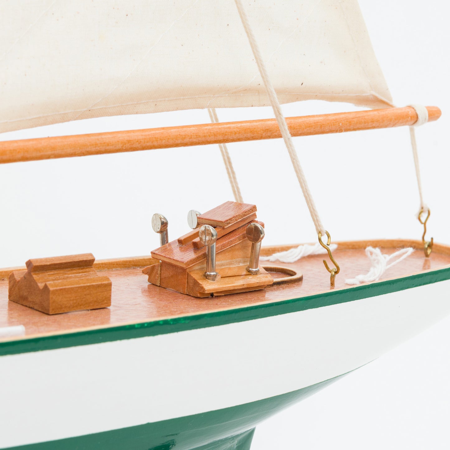 Close-up of a model sailboat with wooden deck and white sails on a white background