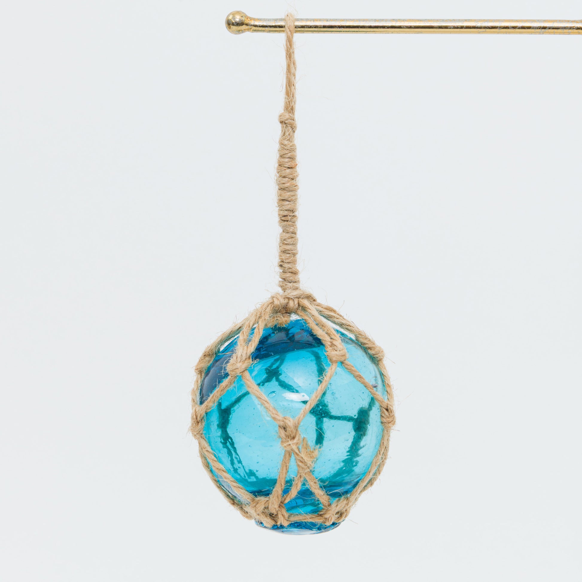 A blue glass ball in a rope net on a white background.