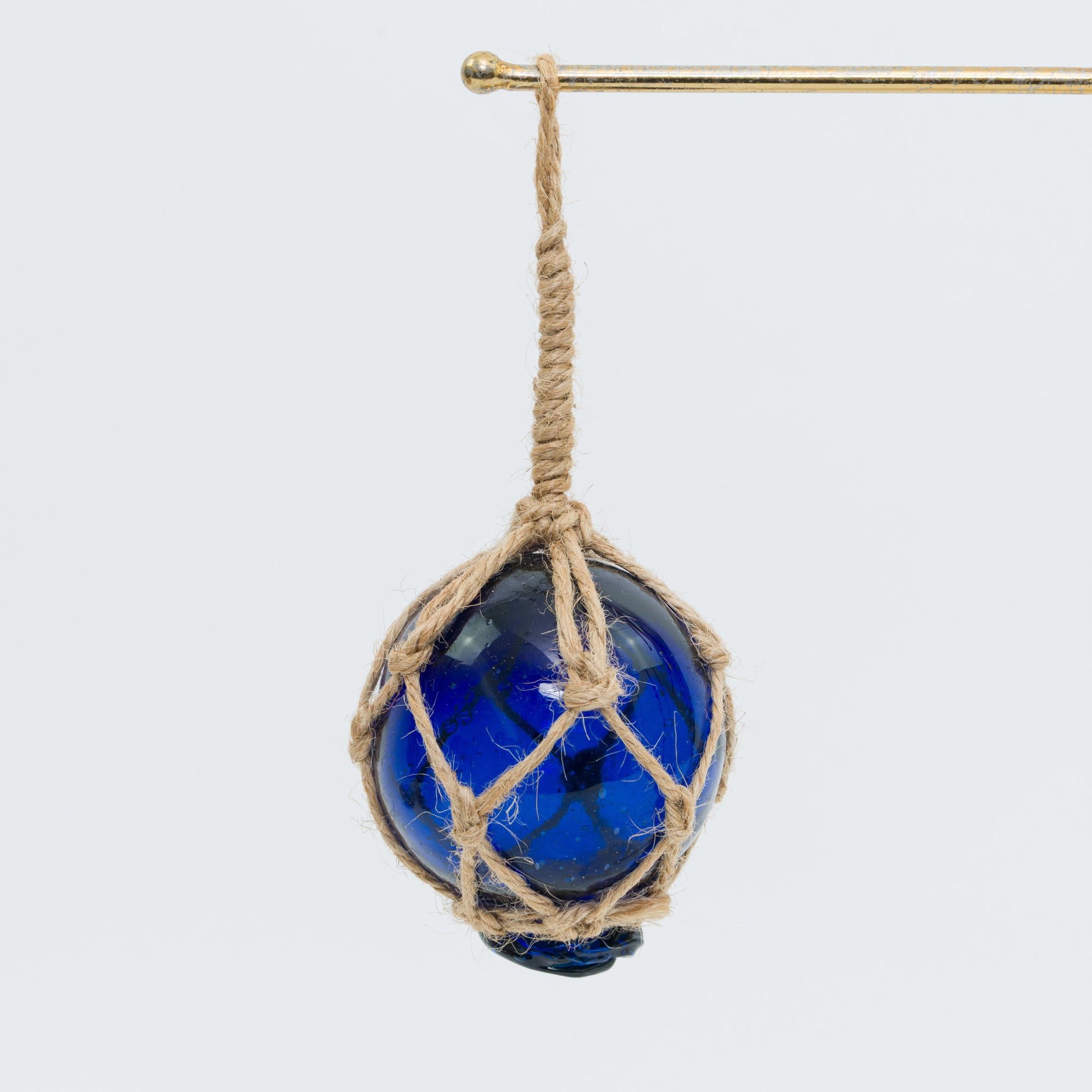 A blue glass buoy with rope netting on a white background