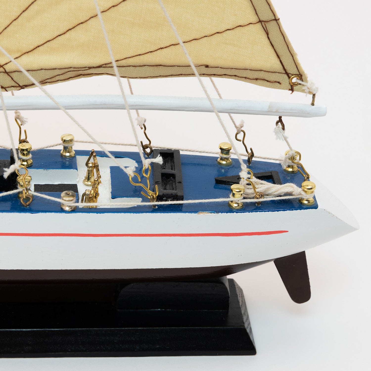 A close-up view of the stern of the model racing yacht with a black and white hull, brass details and tan sails.