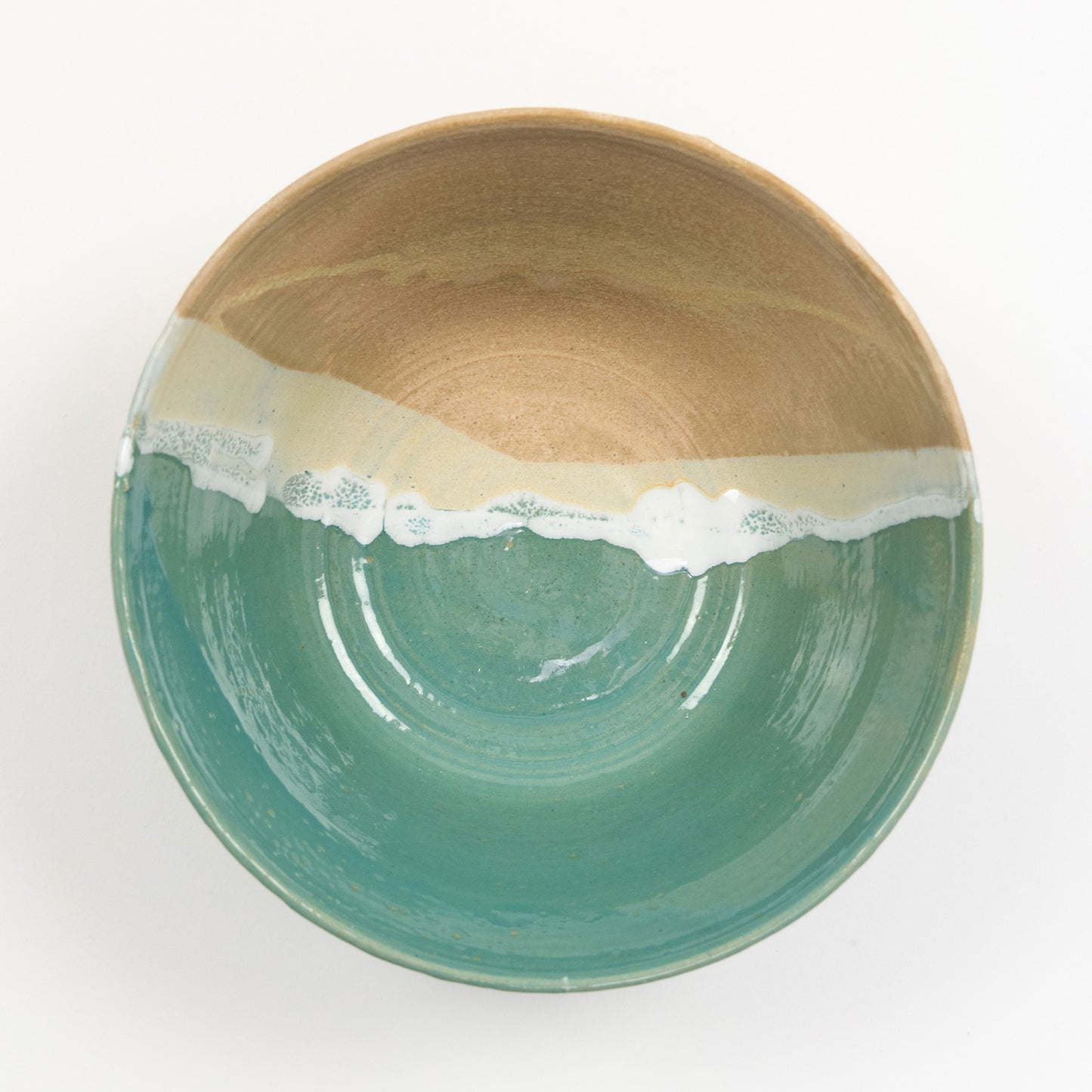 A bowl pictured on a white background. The bowl has an ocean shoreline design, with the sea, a wave, and the sand across it.