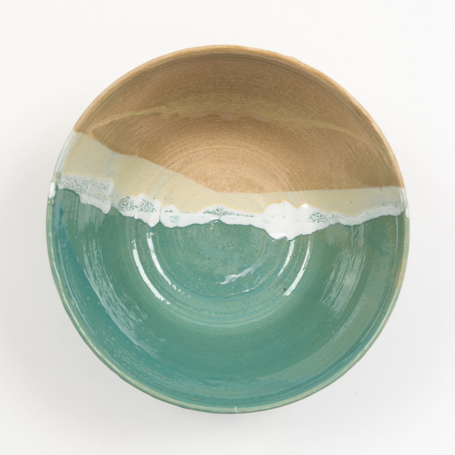 A bowl pictured on a white background. The bowl has an ocean shoreline design, with the sea, a wave, and the sand across it.