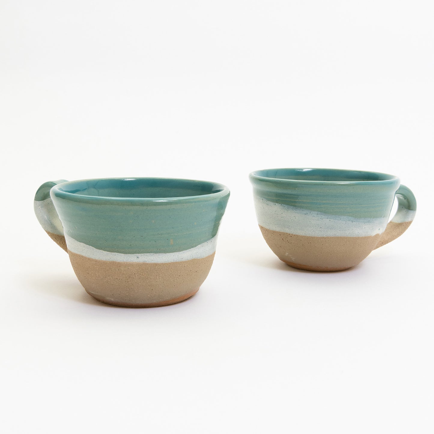 Two mugs featuring an ocean, wave, and shoreline design. Pictured on a white background.