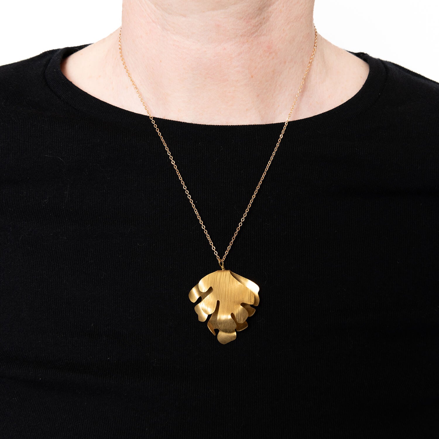 Model wearing brass wave pendant against a black top
