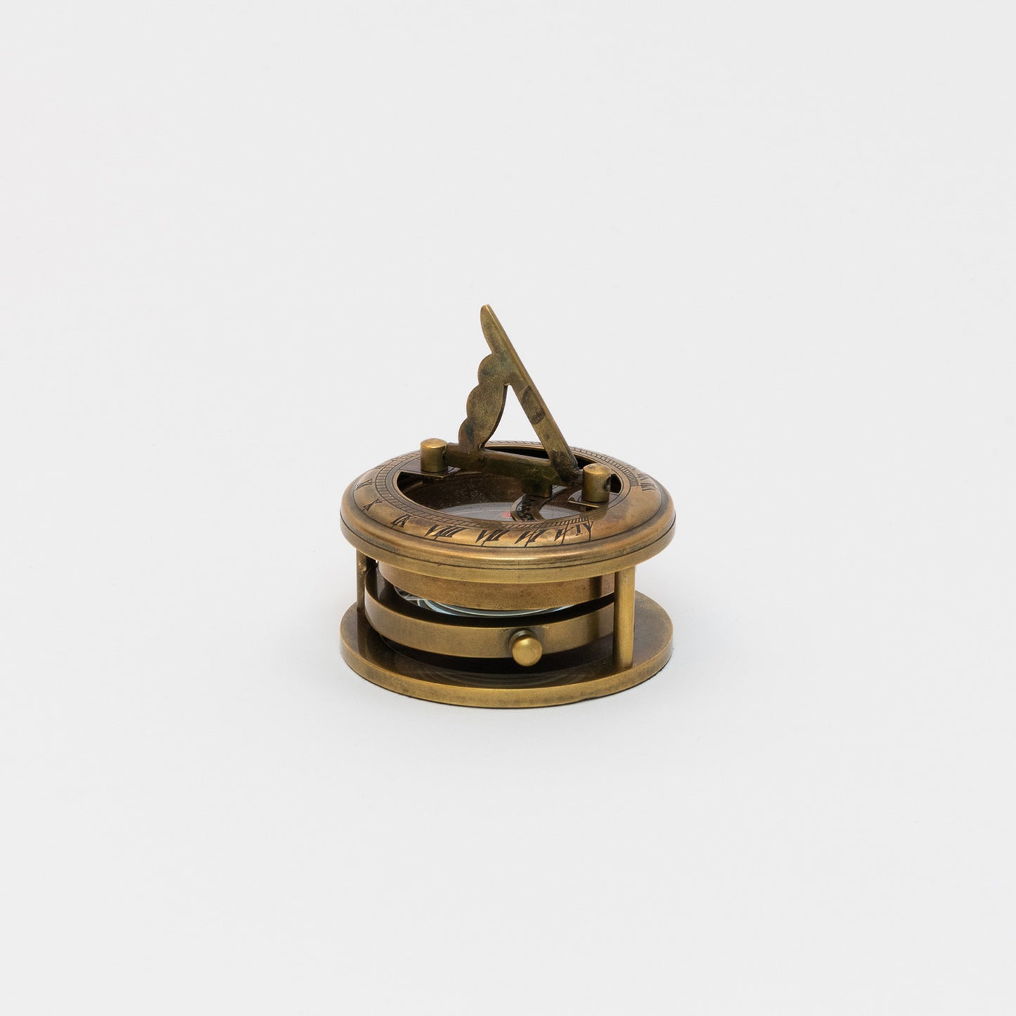 A brass sundial, compass and magnifier chart weight pictured on a white background.