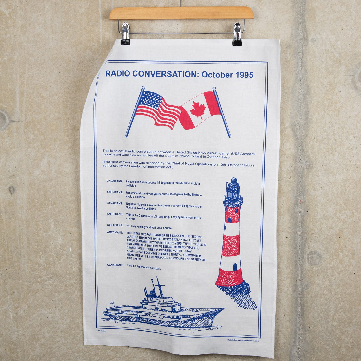 The red, white and blue Conversation Tea Towel hanging from a clothes hanger against a grey background.