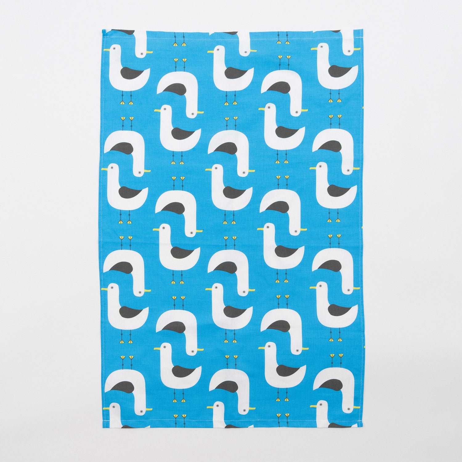 Grey and white seagull illustrations repeat across the blue seagulls tea towel. The seagulls tea towel is on a grey background.