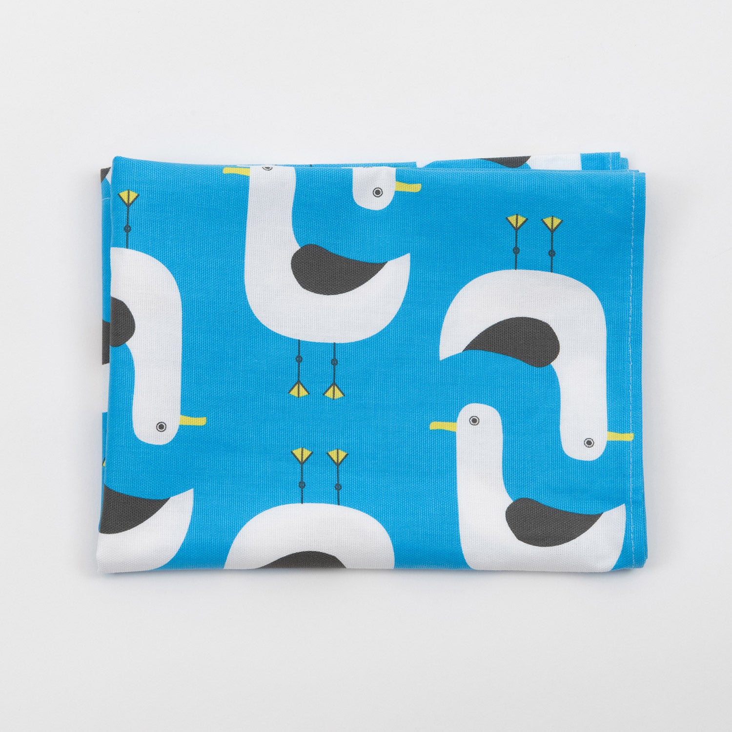 Grey and white seagull illustrations repeat across the blue seagulls tea towel. The seagulls tea towel is folded on a white ackground.