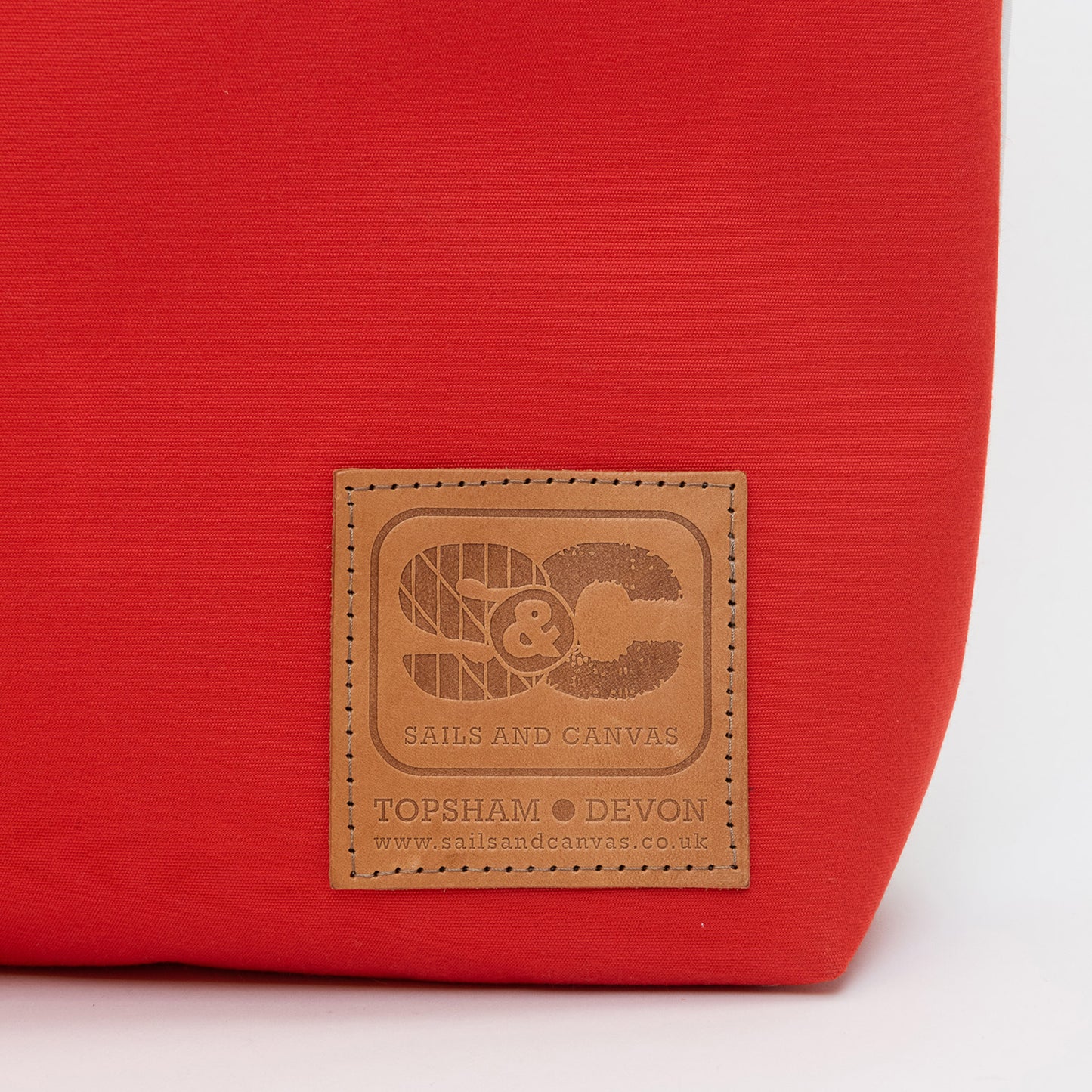 Recycled Sails Tote Bag, close up of leather patch to red base. Stating Sails and Canvas, Topsham Devon.