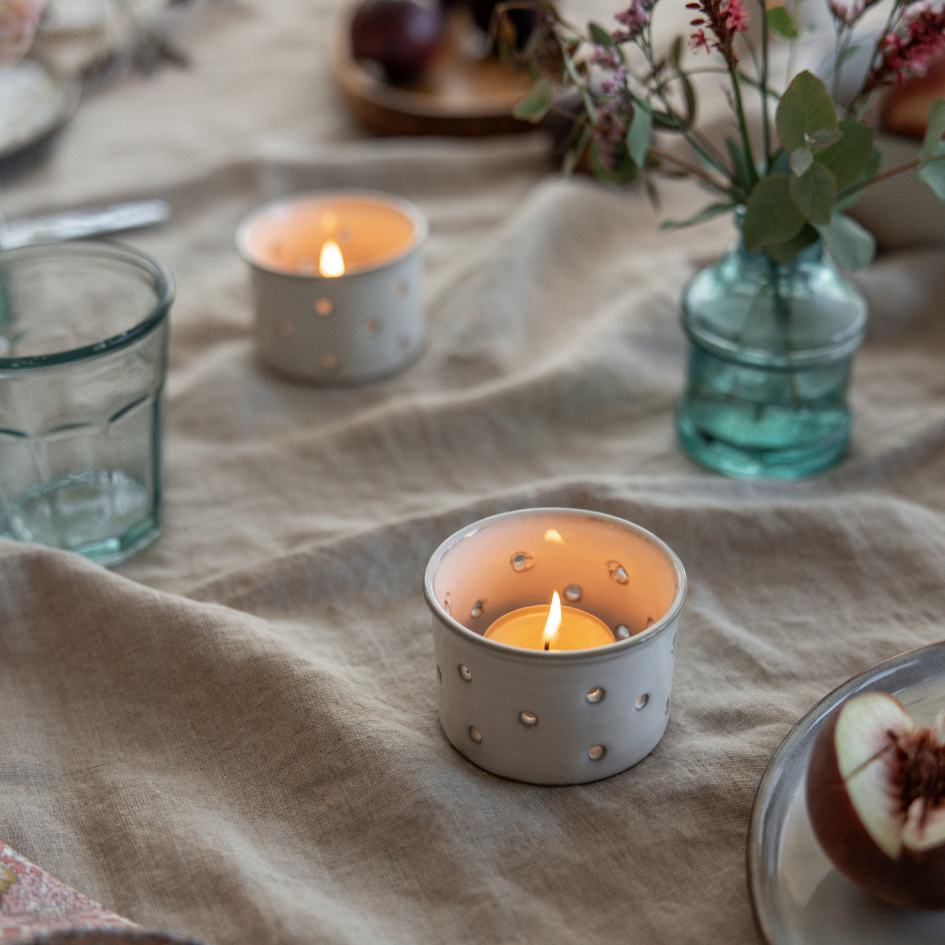 Candlelit scene with small candles in decorative holders on a textured fabric surface.