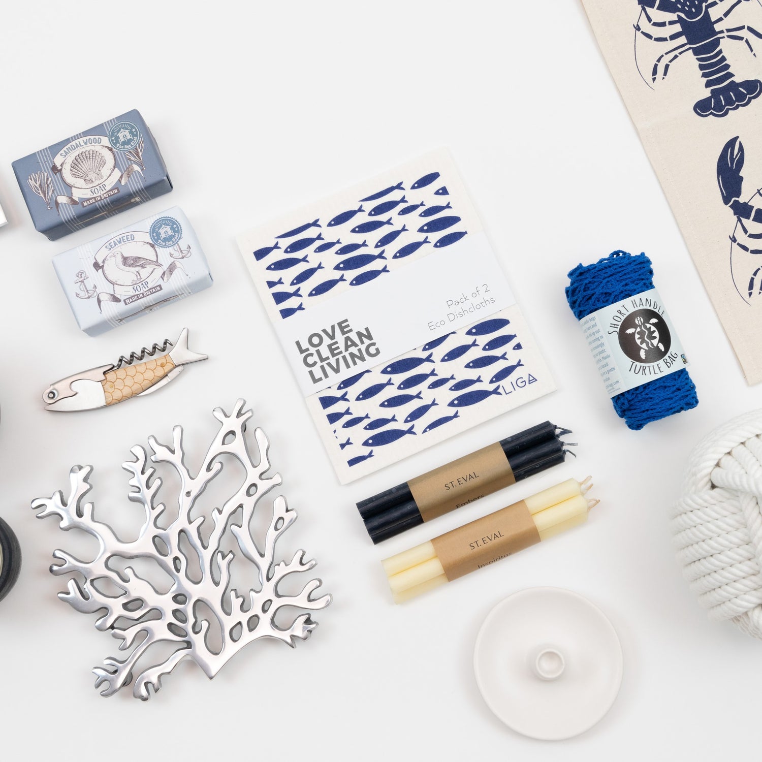 A collection of maritime-themed homeware items arranged on a white table, featuring a tea towel, dish cloth, candles, and soap.
