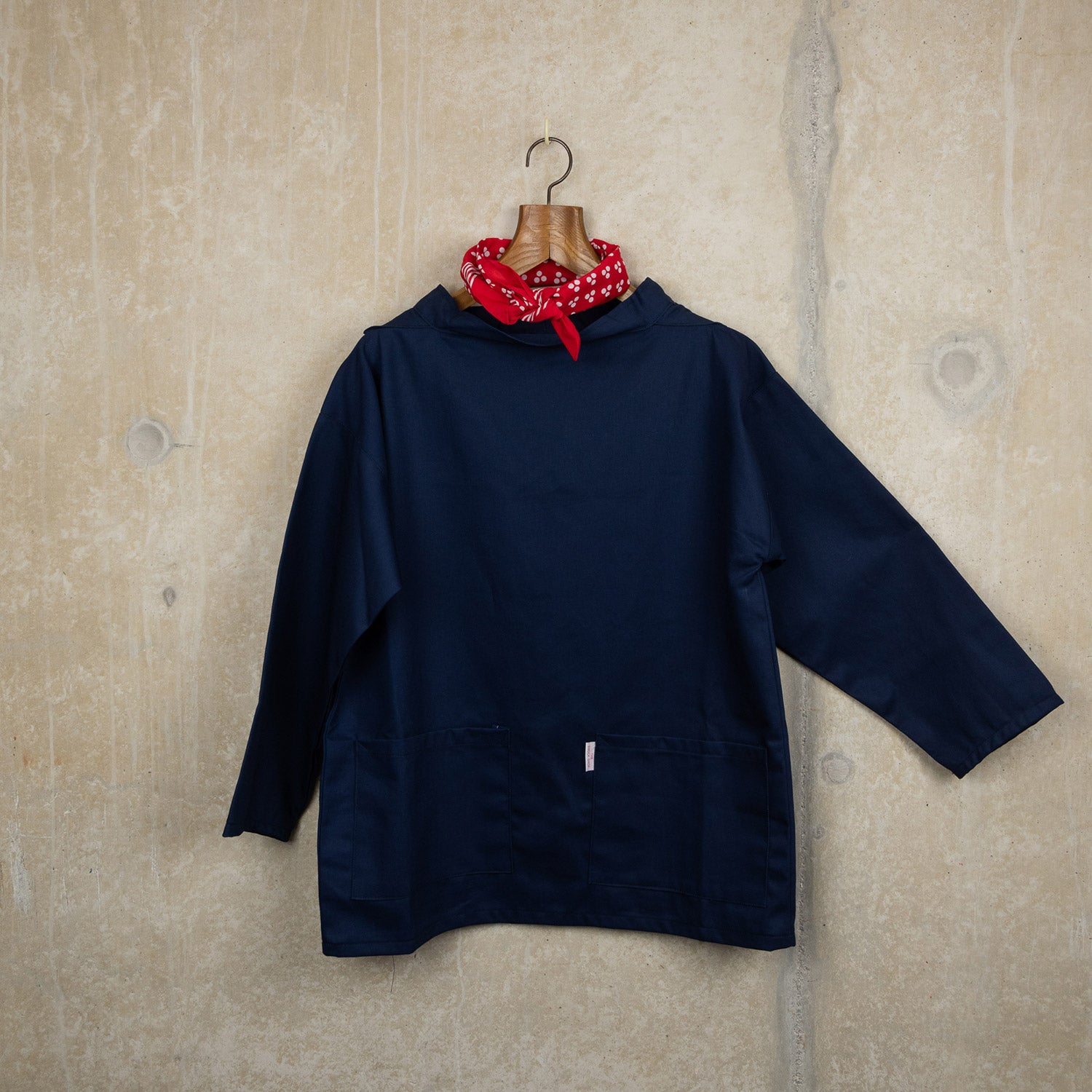 A blue adult smock on a coat hanger, pictured on a rustic concrete background.