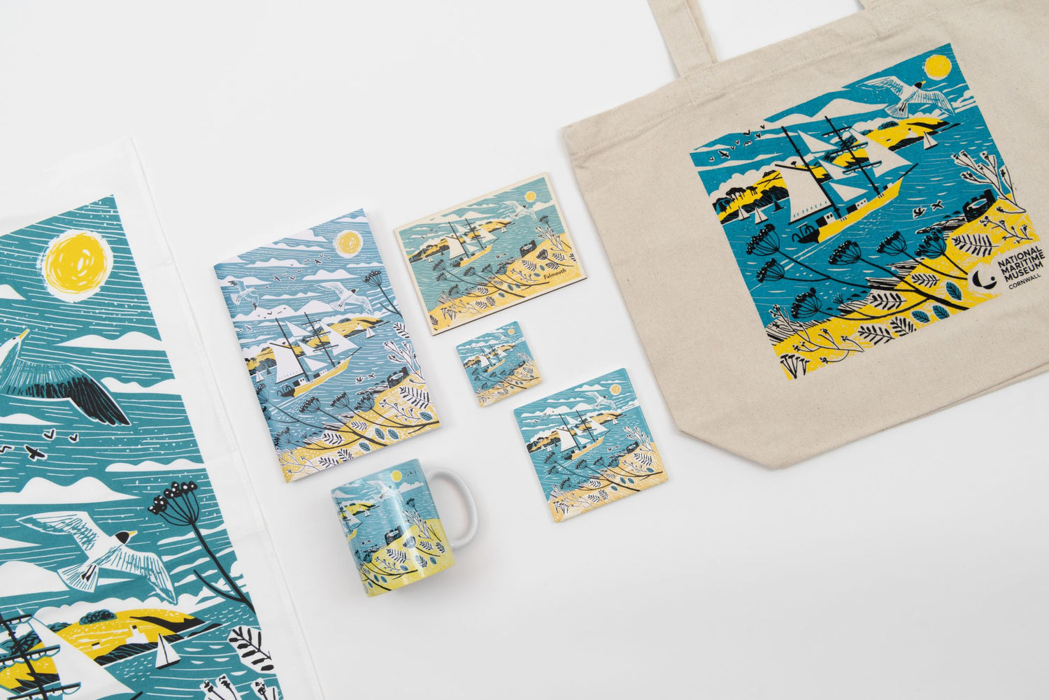 A spread of vibrant products featuring a blue and yellow Falmouth Tall Ships design. There's a tote bag, a mug, coaster, notebook, and magnet.