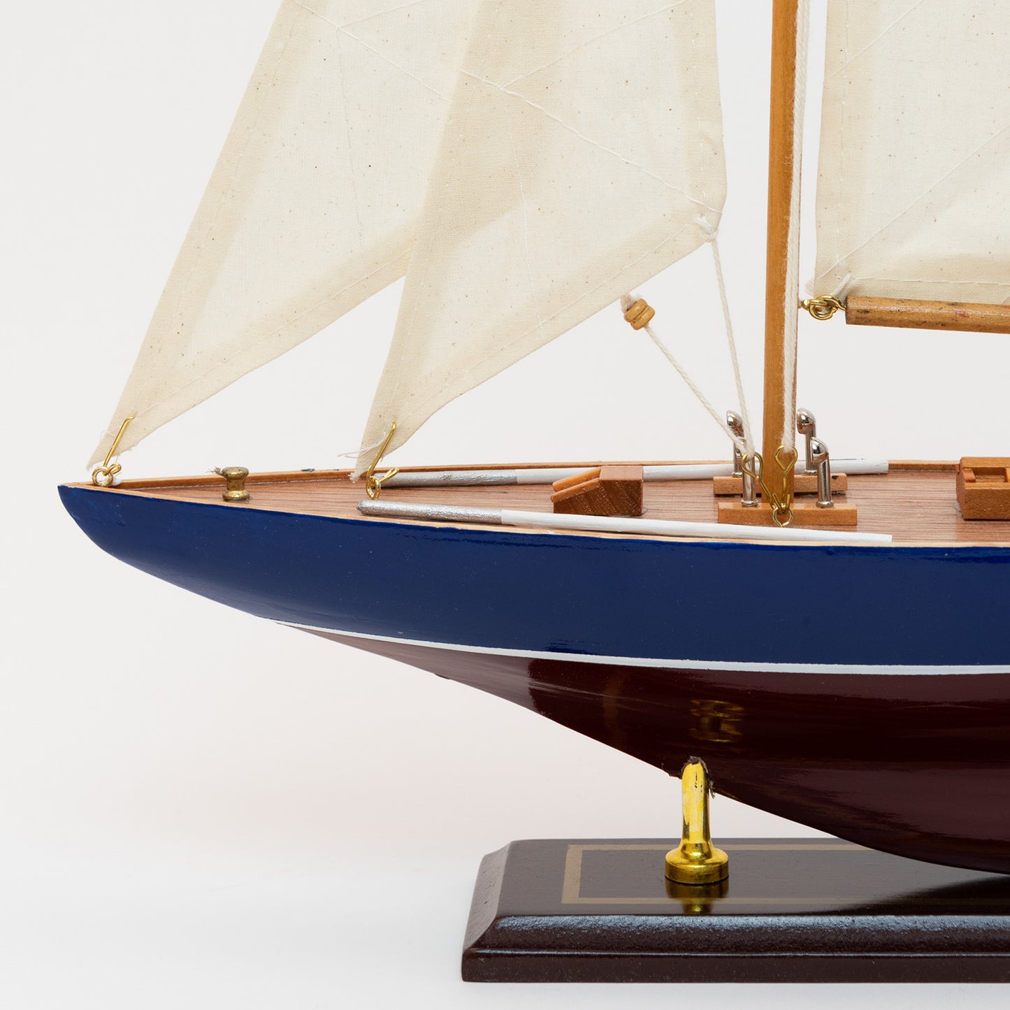 The close-up of the J Class Yacht's bow with a burgundy and blue hull and cream coloured sails. 