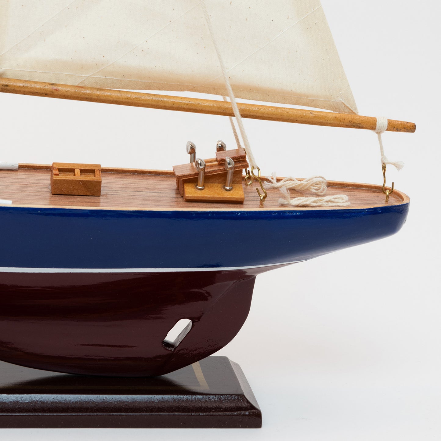 The close-up of the J Class Yacht's stern with a burgundy and blue hull and cream coloured sails. 