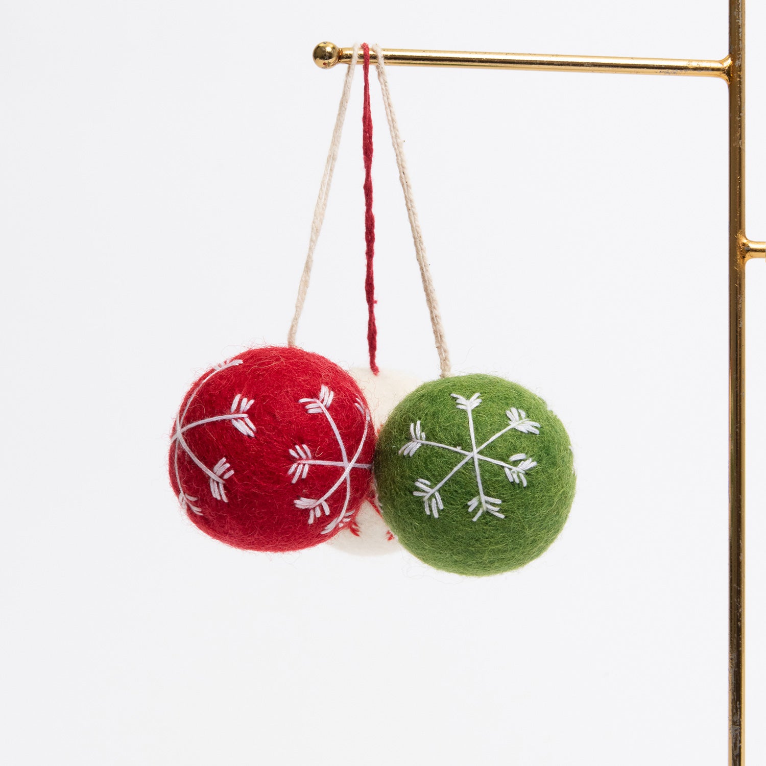 Three felt Christmas bauble decorations hanging on a metal rod. They are white, red, and green, with snowflake stitching on the face of each.