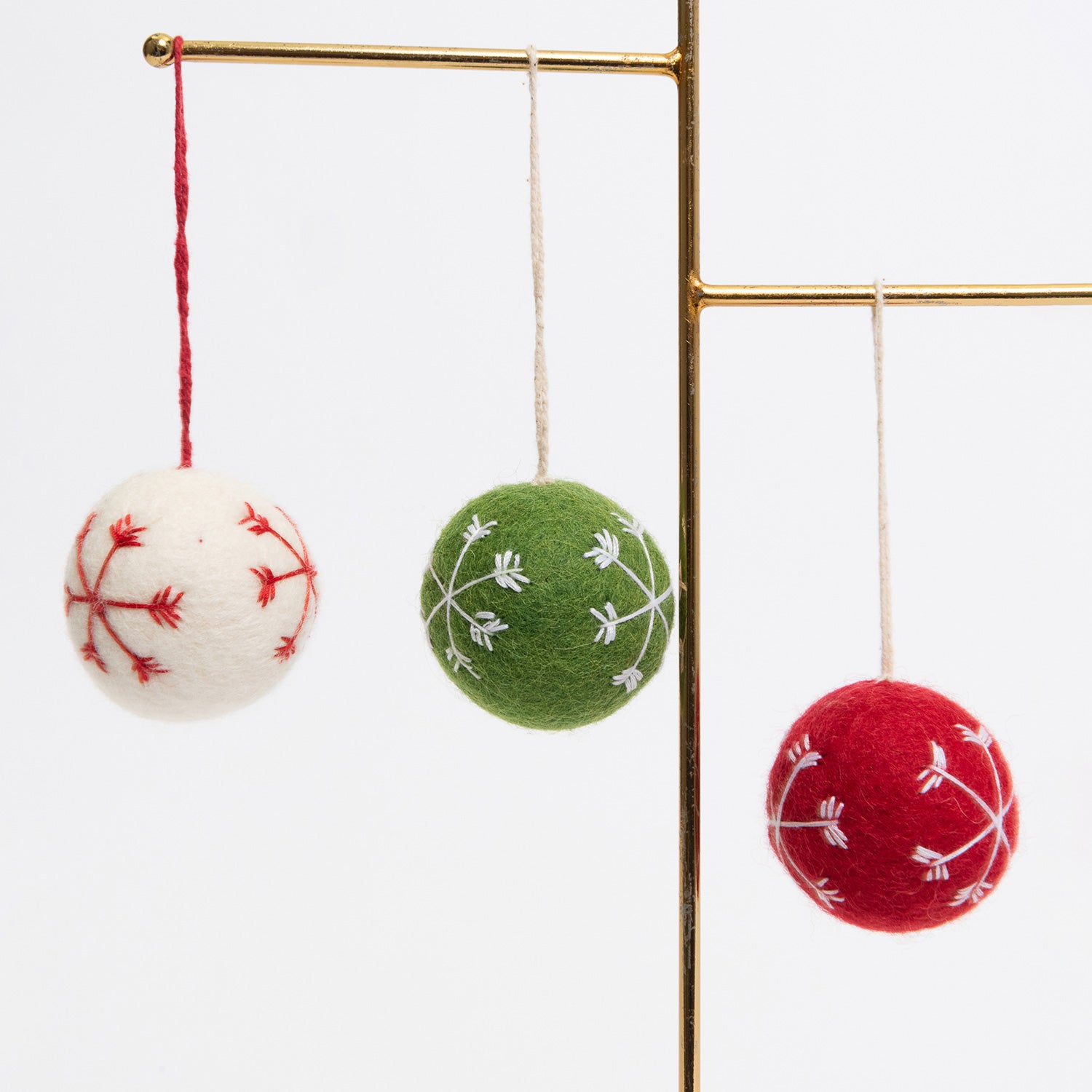Three felt Christmas bauble decorations hanging on a metal rod. They are white, red, and green, with snowflake stitching on the face of each.