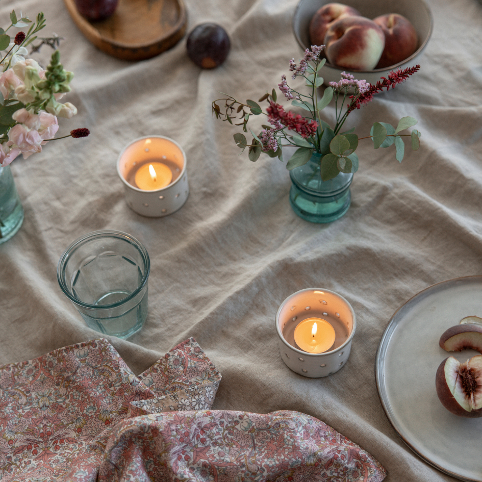 Candlelit table setting with flowers, fruits, and a floral napkin on a textured surface.